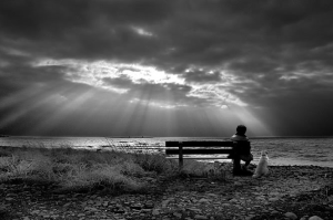 person sitting on a park bench looking at a coming storm
